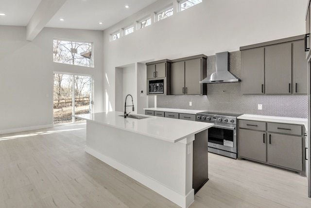 kitchen featuring sink, backsplash, high end stainless steel range oven, an island with sink, and wall chimney exhaust hood