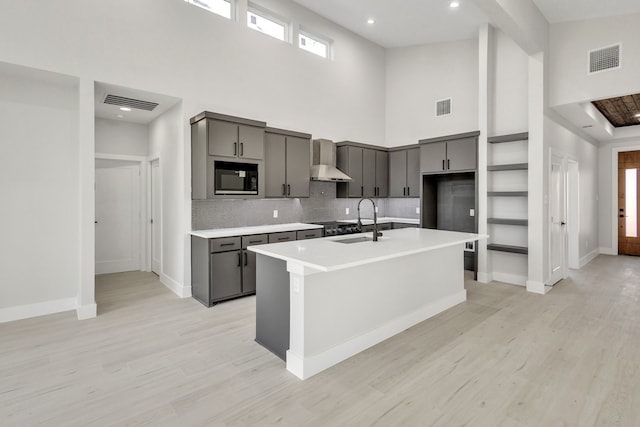 kitchen featuring sink, a high ceiling, a kitchen island with sink, wall chimney range hood, and black microwave