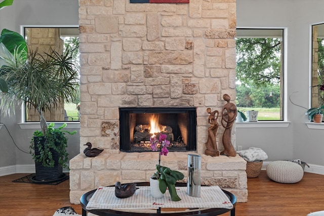 living area featuring a stone fireplace, baseboards, and wood finished floors