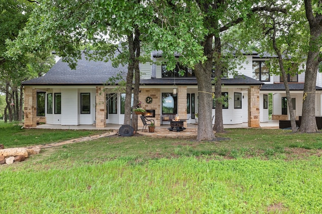 rear view of property featuring a patio area, roof with shingles, a fire pit, and a yard