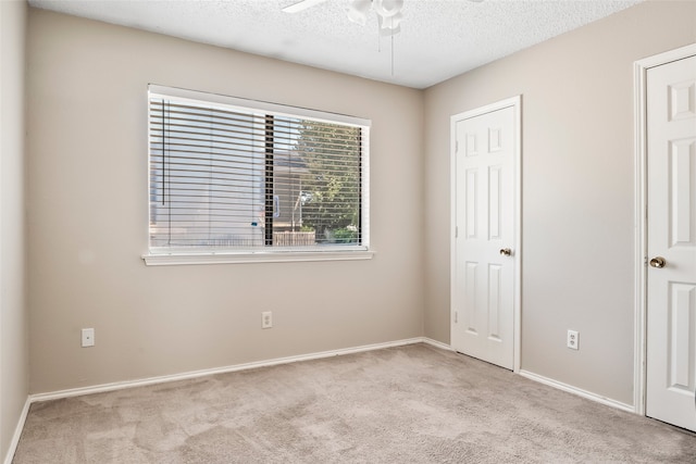 unfurnished bedroom with ceiling fan, light colored carpet, and a textured ceiling