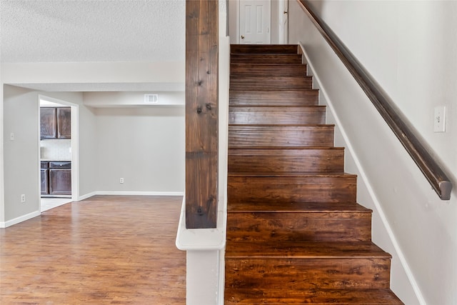 staircase with hardwood / wood-style floors and a textured ceiling