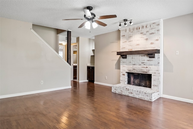 unfurnished living room featuring a fireplace, rail lighting, wood-type flooring, a textured ceiling, and ceiling fan