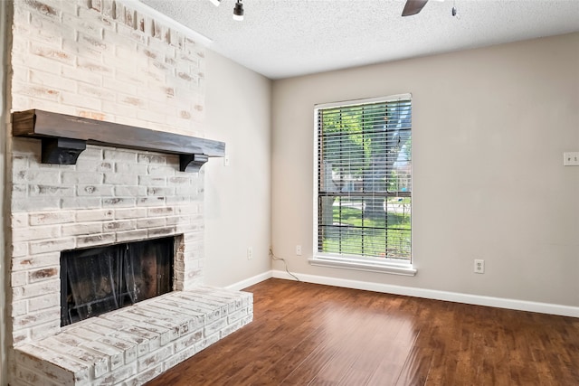 unfurnished living room with a textured ceiling, brick wall, dark hardwood / wood-style floors, and a brick fireplace