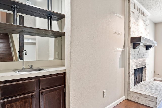 bathroom featuring wood-type flooring, a textured ceiling, a brick fireplace, and vanity