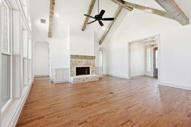 unfurnished living room with light hardwood / wood-style flooring, ceiling fan, beam ceiling, a stone fireplace, and high vaulted ceiling