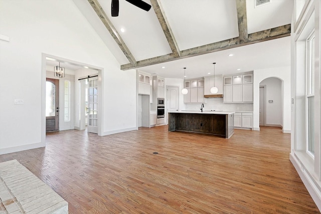 unfurnished living room with light hardwood / wood-style floors, beamed ceiling, high vaulted ceiling, and ceiling fan