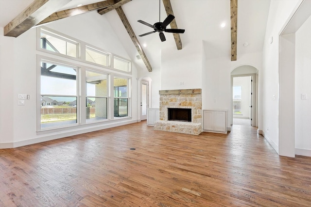 unfurnished living room featuring wood-type flooring, beamed ceiling, a fireplace, ceiling fan, and high vaulted ceiling