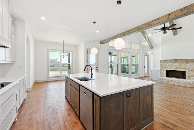 kitchen with a stone fireplace, light hardwood / wood-style floors, dishwasher, sink, and decorative light fixtures