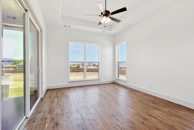 spare room featuring hardwood / wood-style flooring, a raised ceiling, ceiling fan, and a healthy amount of sunlight