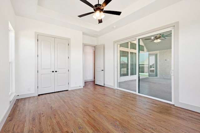 unfurnished bedroom with ceiling fan, light hardwood / wood-style flooring, access to outside, and a tray ceiling