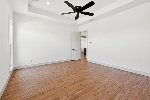 spare room featuring ceiling fan, a raised ceiling, and light wood-type flooring