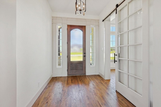 entrance foyer featuring wood-type flooring, an inviting chandelier, and a barn door