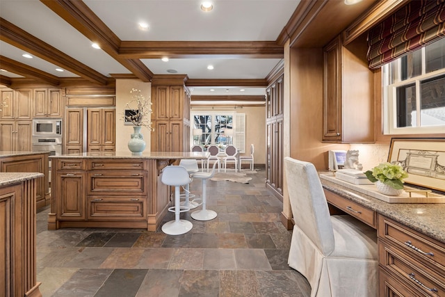 kitchen featuring a breakfast bar area, stainless steel microwave, built in desk, ornamental molding, and beamed ceiling