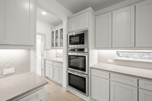 kitchen featuring light hardwood / wood-style floors, white cabinetry, backsplash, and stainless steel microwave