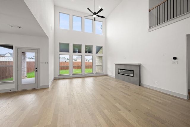 unfurnished living room featuring light hardwood / wood-style flooring, a tiled fireplace, ceiling fan, and a towering ceiling