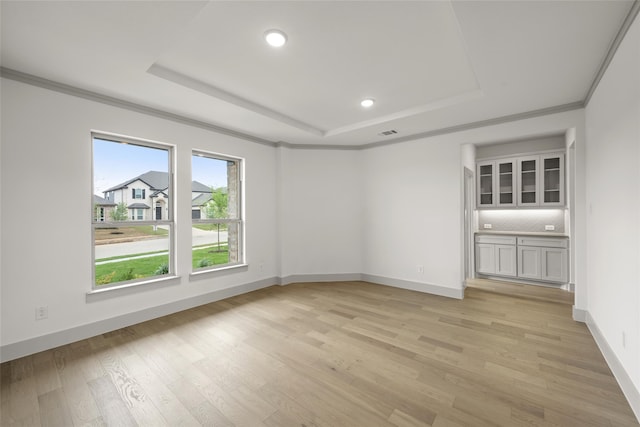 spare room featuring light hardwood / wood-style floors, a raised ceiling, and ornamental molding