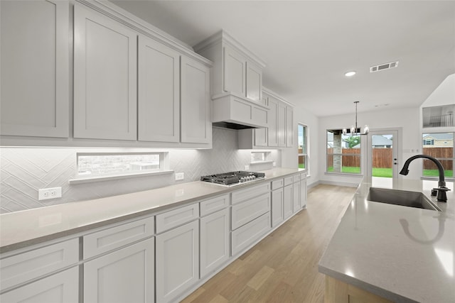 kitchen featuring tasteful backsplash, stainless steel gas stovetop, light wood-type flooring, sink, and white cabinets