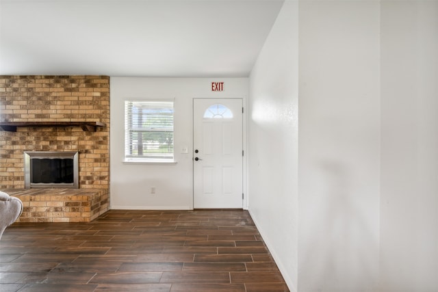 entrance foyer with dark hardwood / wood-style flooring, brick wall, and a brick fireplace