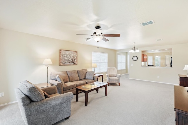 carpeted living room with ceiling fan with notable chandelier