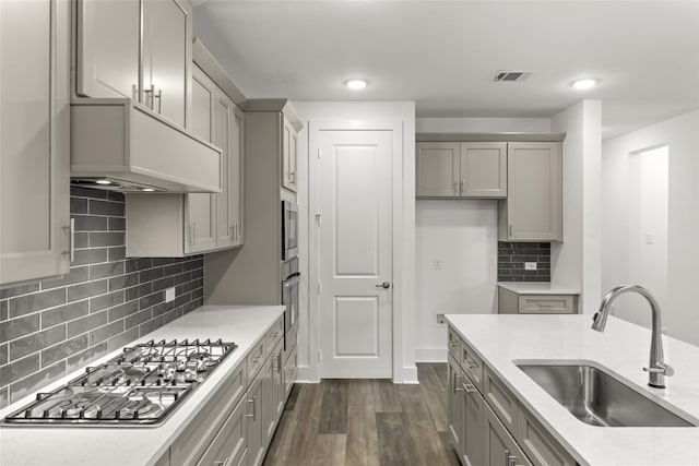 kitchen featuring appliances with stainless steel finishes, light stone countertops, backsplash, sink, and dark wood-type flooring