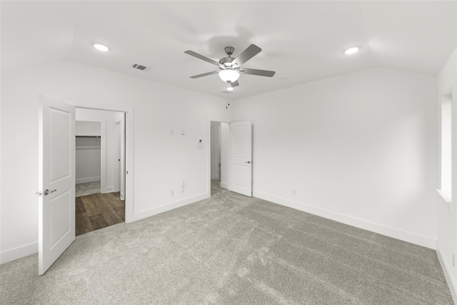 unfurnished bedroom featuring ceiling fan, carpet, vaulted ceiling, and a walk in closet