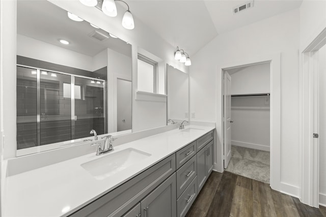 bathroom featuring vaulted ceiling, double vanity, a shower with door, and hardwood / wood-style flooring