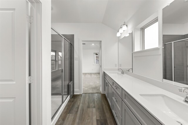 bathroom featuring walk in shower, dual bowl vanity, vaulted ceiling, and wood-type flooring