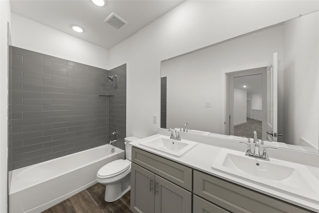 full bathroom with wood-type flooring, dual bowl vanity, toilet, and tiled shower / bath