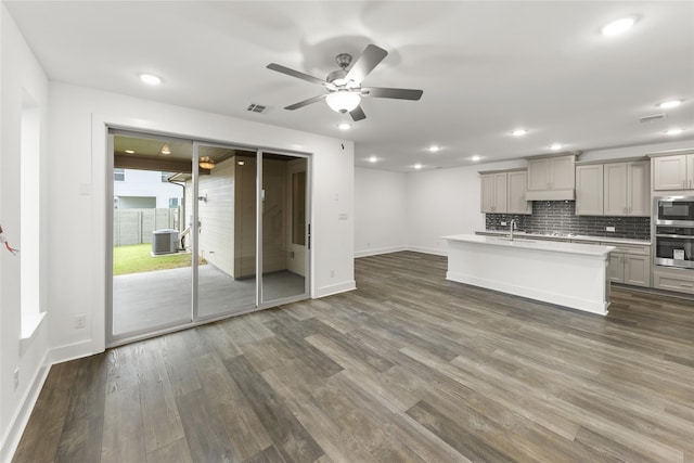 kitchen featuring ceiling fan, dark wood-type flooring, a center island with sink, backsplash, and stainless steel appliances