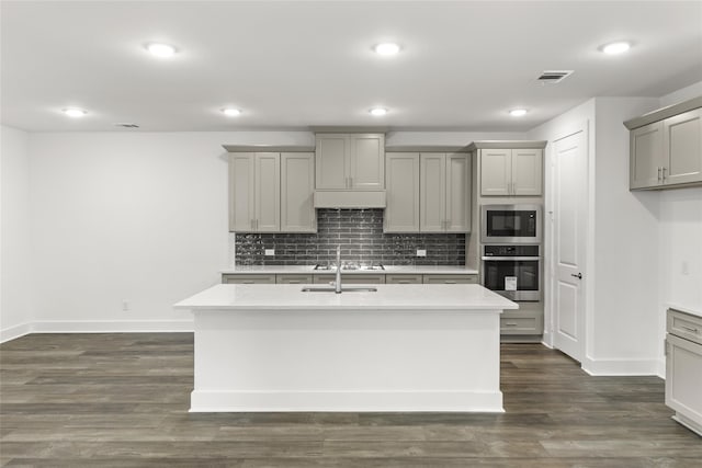 kitchen with appliances with stainless steel finishes, dark wood-type flooring, an island with sink, and gray cabinetry