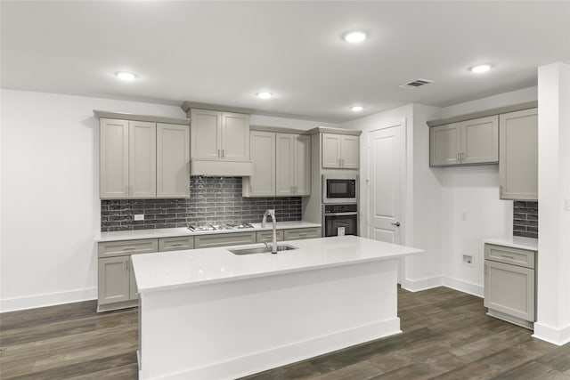 kitchen featuring dark wood-type flooring, premium range hood, appliances with stainless steel finishes, a center island with sink, and sink