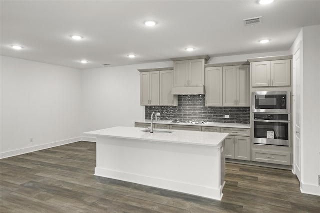 kitchen with appliances with stainless steel finishes, dark wood-type flooring, backsplash, and a kitchen island with sink