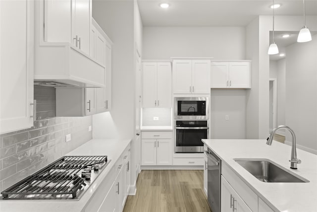 kitchen featuring light wood-type flooring, backsplash, hanging light fixtures, sink, and appliances with stainless steel finishes