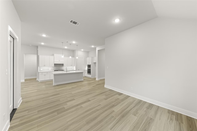 unfurnished living room with sink, light hardwood / wood-style floors, and vaulted ceiling