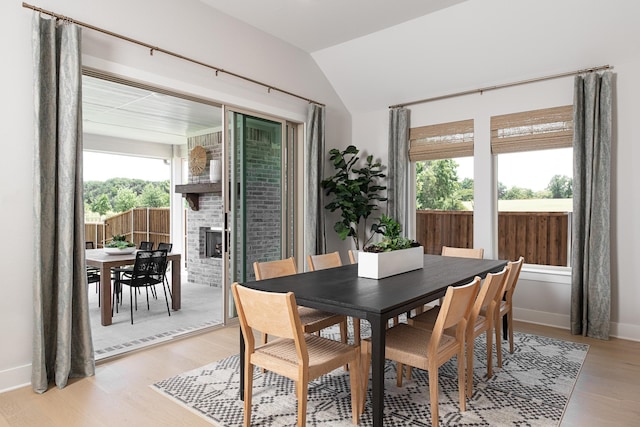 dining space featuring a healthy amount of sunlight, a fireplace, light wood-type flooring, and vaulted ceiling