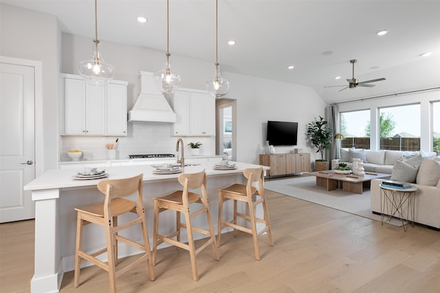 kitchen with white cabinetry, light hardwood / wood-style flooring, backsplash, ceiling fan, and custom exhaust hood