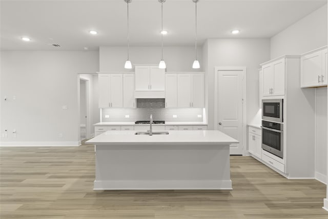 kitchen with light hardwood / wood-style floors, tasteful backsplash, decorative light fixtures, oven, and a kitchen island with sink