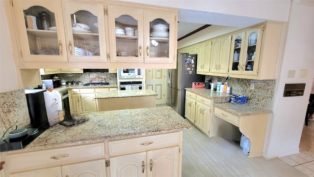 kitchen featuring light stone countertops, appliances with stainless steel finishes, a kitchen island, tasteful backsplash, and light hardwood / wood-style floors