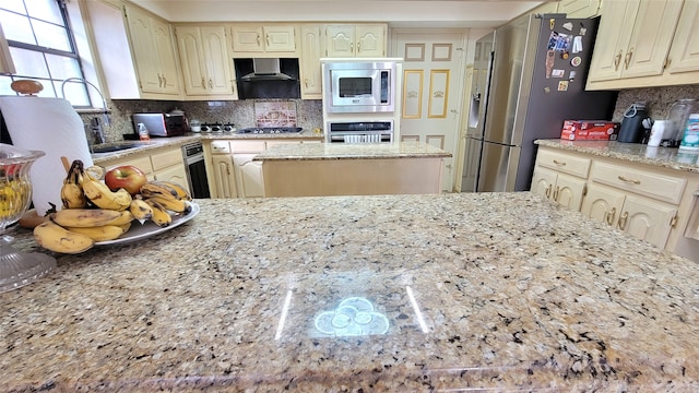 kitchen with a center island, light stone countertops, backsplash, appliances with stainless steel finishes, and wall chimney range hood