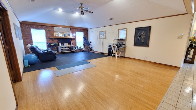 workout room featuring ceiling fan, light tile flooring, lofted ceiling, brick wall, and crown molding