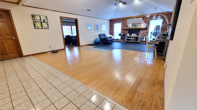 living room with brick wall, vaulted ceiling, light hardwood / wood-style flooring, and ceiling fan