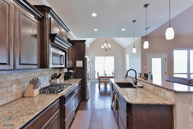 kitchen featuring decorative light fixtures, backsplash, stainless steel appliances, a kitchen island with sink, and sink