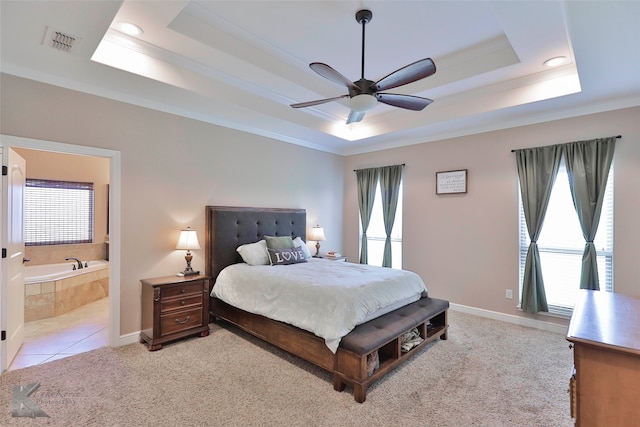 carpeted bedroom with a raised ceiling, multiple windows, ceiling fan, and ensuite bath