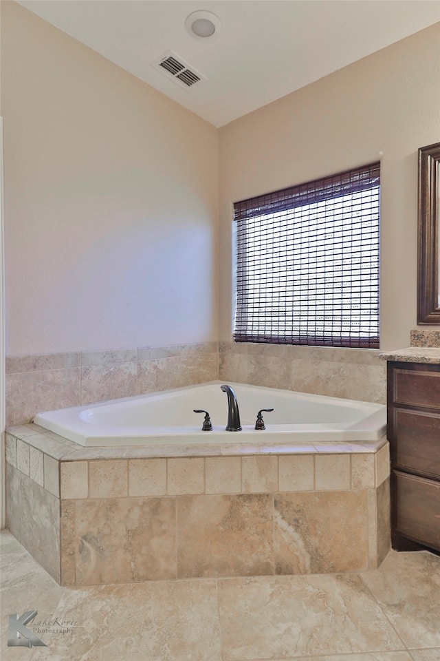 bathroom with tile flooring, tiled tub, and vanity