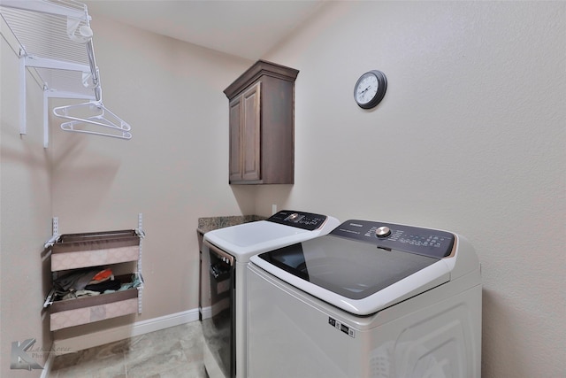 clothes washing area with cabinets, light tile floors, and washer and clothes dryer