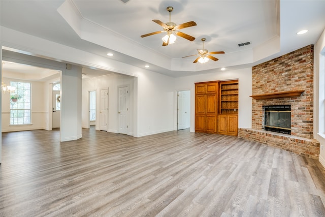 unfurnished living room featuring a brick fireplace, light hardwood / wood-style floors, and a tray ceiling