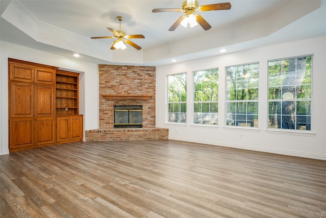 unfurnished living room with ornamental molding, ceiling fan, a raised ceiling, light hardwood / wood-style flooring, and a brick fireplace