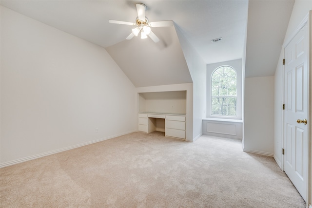 additional living space with light colored carpet, ceiling fan, built in desk, and vaulted ceiling