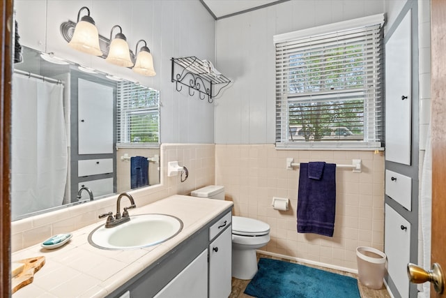 bathroom featuring tile walls, toilet, large vanity, and a wealth of natural light